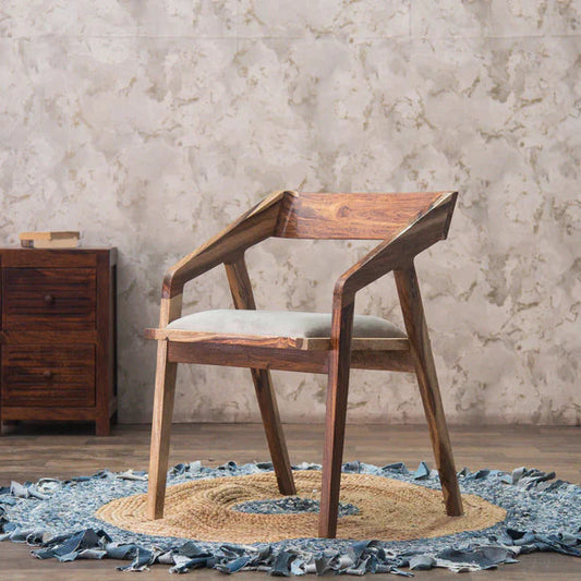 Wooden chair with a white cushion on a textured rug in a room with a stone wall.
