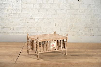 Wooden coffee table with a floral design on a wooden floor against a white brick wall.
