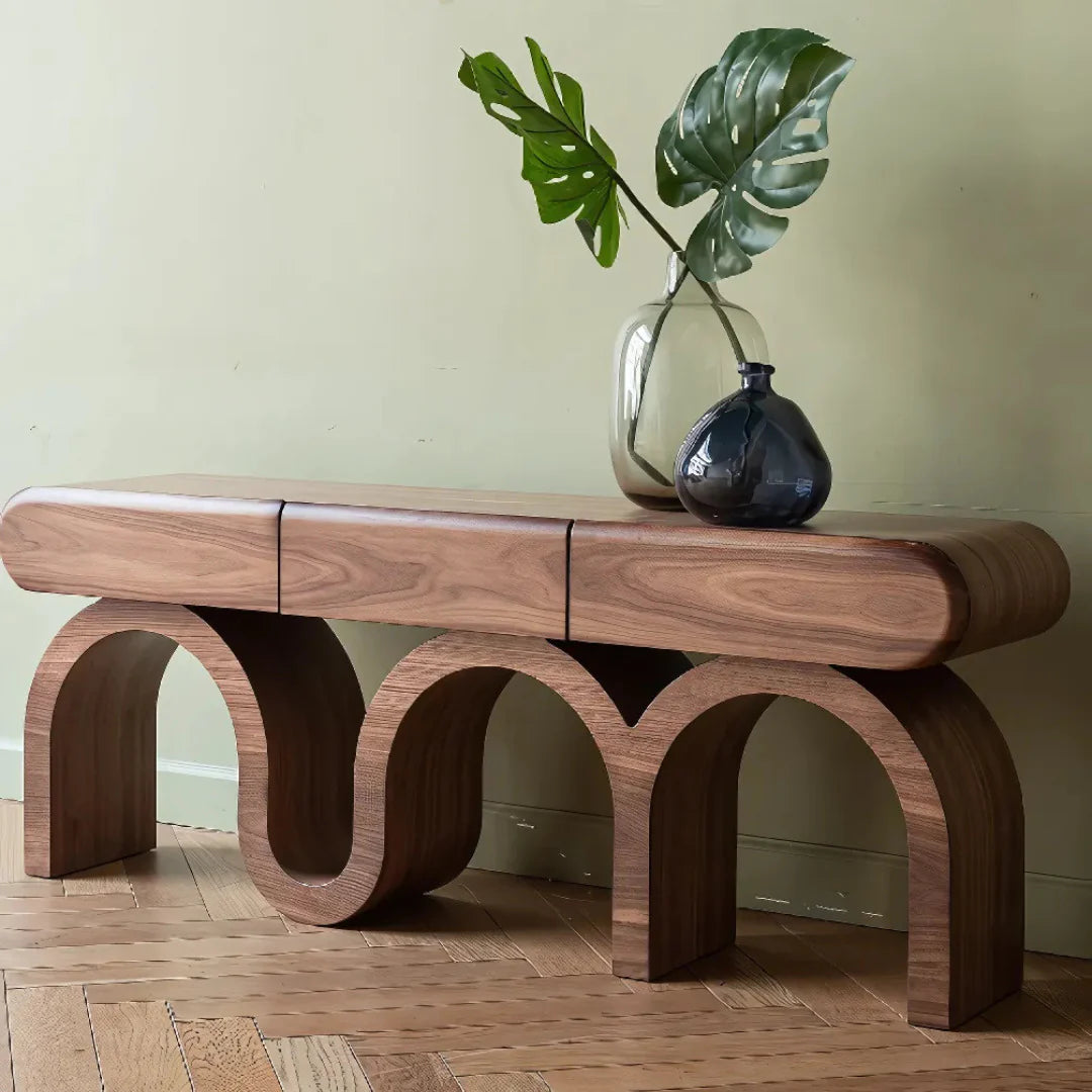 Wooden bench with arches on a wooden floor, featuring a vase with green leaves.