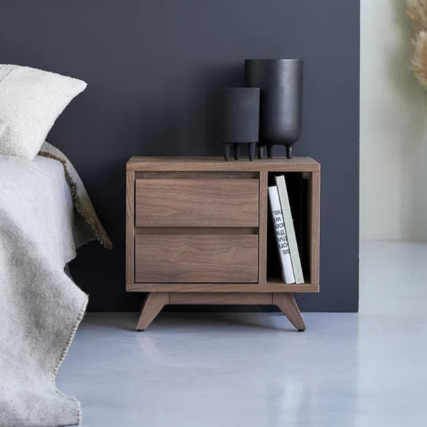 Wooden nightstand with books and lamps against a dark wall in a bedroom setting.