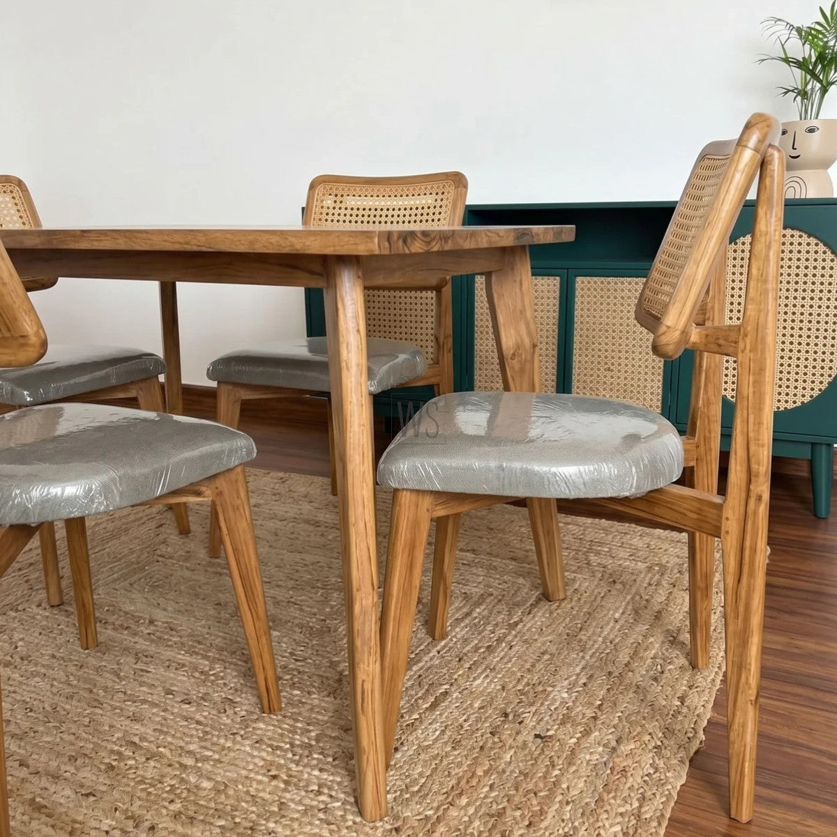 Dining table with wooden chairs and gray cushioned seats on a textured rug.