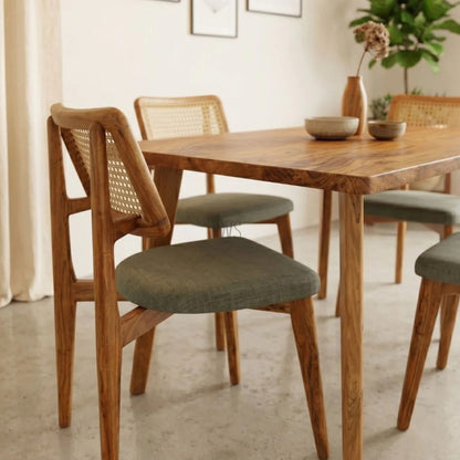 Dining table with wooden chairs and green cushioned seats in a room with light-colored walls.
