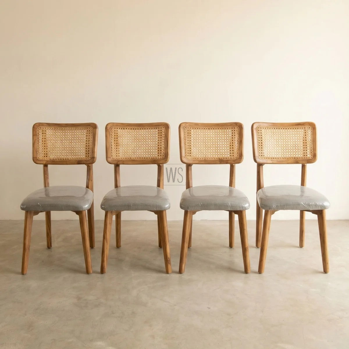 Four wooden chairs with wicker backrests and gray seats on a beige floor.